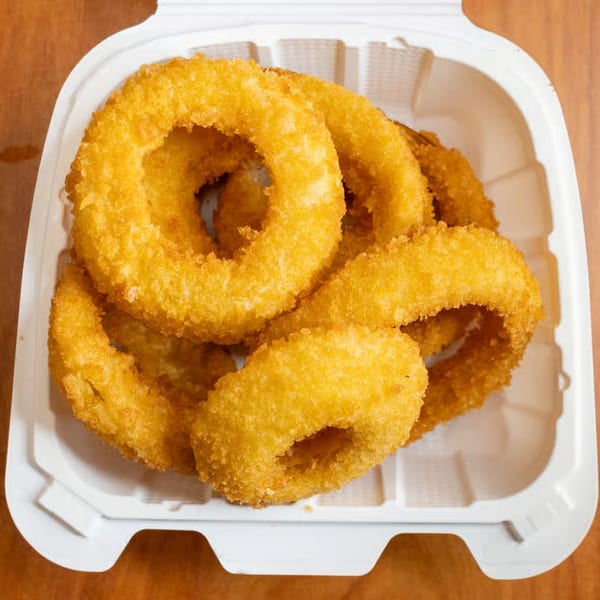 Golden-brown, crispy onion rings from Milan's Real Philly Cheesesteaks and Hoagies, served in a white takeout container.