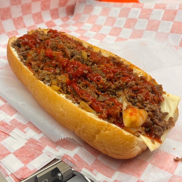 A Milan's Real Philly Cheesesteak with steak, onions, cheese, and ketchup on a hoagie roll.
