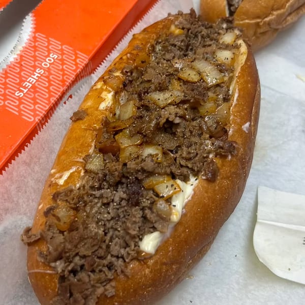 A Milan's Real Philly Cheesesteak, loaded with steak, onions, and cheese, on a white paper.