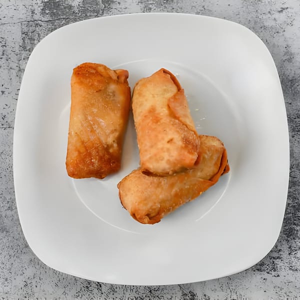 Three golden-brown Milan's Real Philly Cheesesteaks egg rolls are arranged on a white square plate.