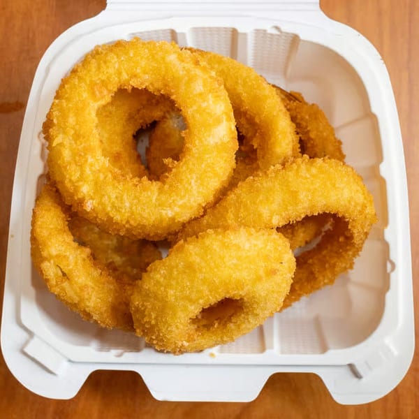 Golden-brown onion rings from Milan's Real Philly Cheesesteaks and Hoagies, served in a white takeout container.
