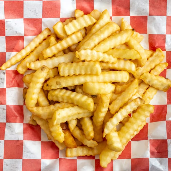 A pile of golden, crinkle-cut french fries rests on red and white checkered paper.