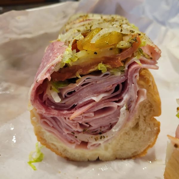A Milan's Real Philly Hoagie, sliced open, revealing layers of deli meats, cheese, lettuce, and pickles.