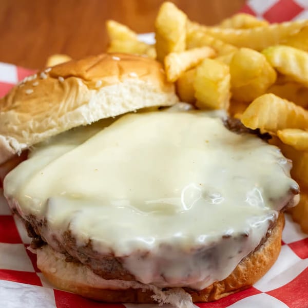 A Milan's cheesesteak with melted cheese and a side of crinkle-cut fries in a red and white basket.
